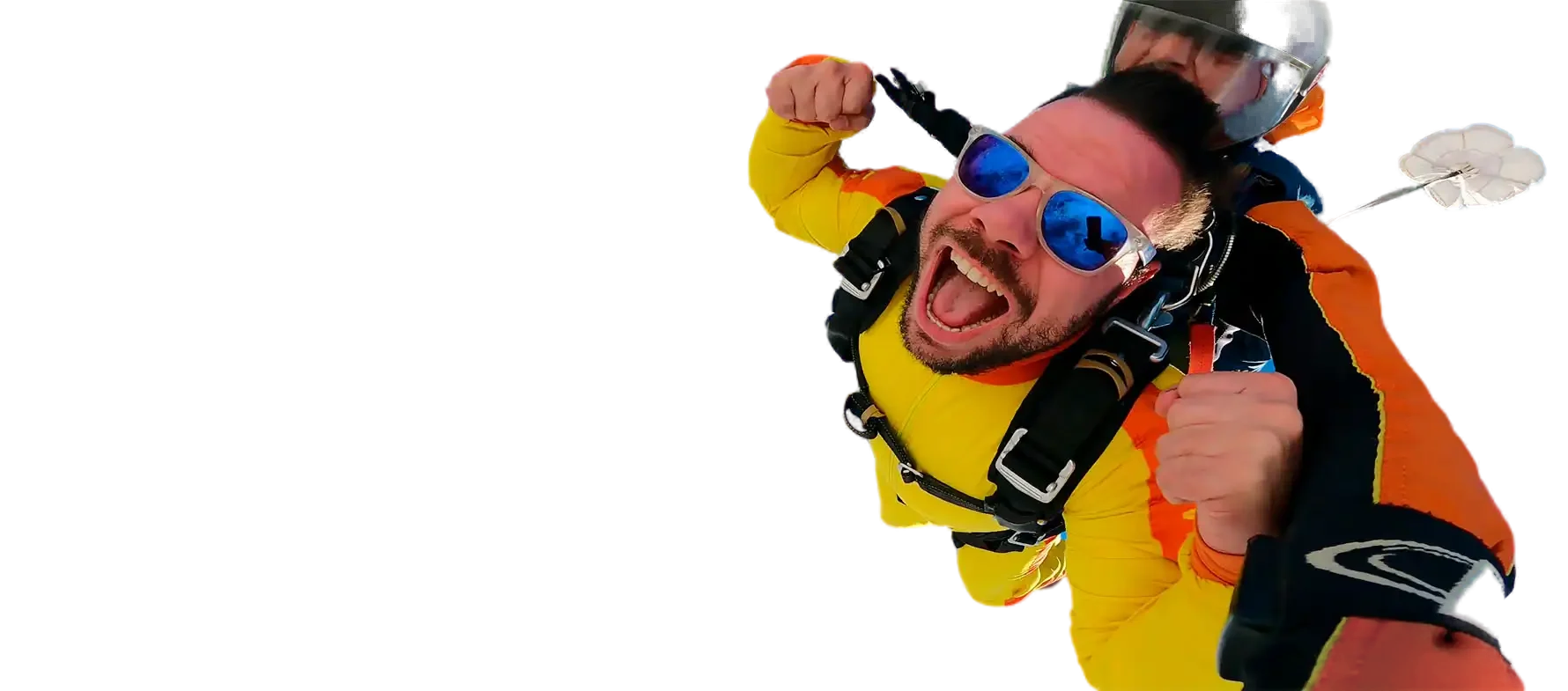 Marco Rodrigues em queda livre num salto de paraquedas em tandem, de fato amarelo e óculos de sol espelhados, a gritar de alegria com o punho no ar.